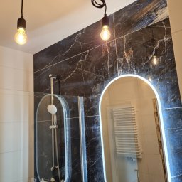 Slawomir S-Bygg - Nowoczesna łazienka z kabiną prysznicową i podświetlanym lustrem na tle płytek imitujących marmur. Dwie wiszące lampy z żarówkami Edisona.