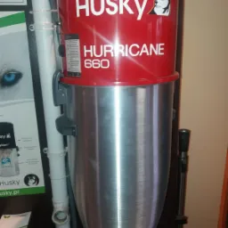 Stacjonarny odkurzacz centralny Husky Hurricane 660 z czerwono-srebrną obudową, widoczny przewód instalacyjny i materiały reklamowe producenta