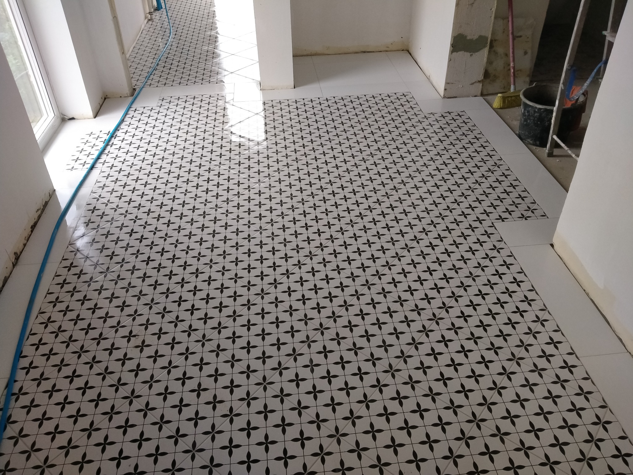 Układanie wzorzystych, czarno-białych płytek podłogowych w trakcie remontu, widoczne niedokończone fragmenty i narzędzia budowlane.