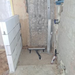 „JUPINEX “ Adam Jueppner - Wnętrze łazienki w trakcie remontu: widoczne bloczki Ytong, odpływ liniowy, poziomica, puszka pod baterię, pianka montażowa i fragment instalacji wodnej.
