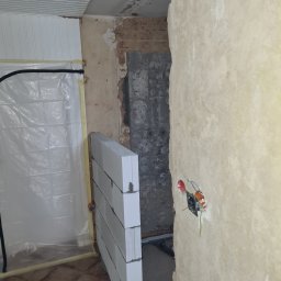 „JUPINEX “ Adam Jueppner - Wnętrze w trakcie prac: ściana z pustaków, zabezpieczona folią strefa, widoczne przewody elektryczne. Fragment sufitu z boazerią. Etap budowy lub remontu.