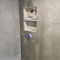 „JUPINEX “ Adam Jueppner - Ściana w trakcie szpachlowania z wnęką i puszką elektryczną. Widoczne ślady szpachli i niedoskonałości, co wskazuje na etap prac wykończeniowych w pomieszczeniu.