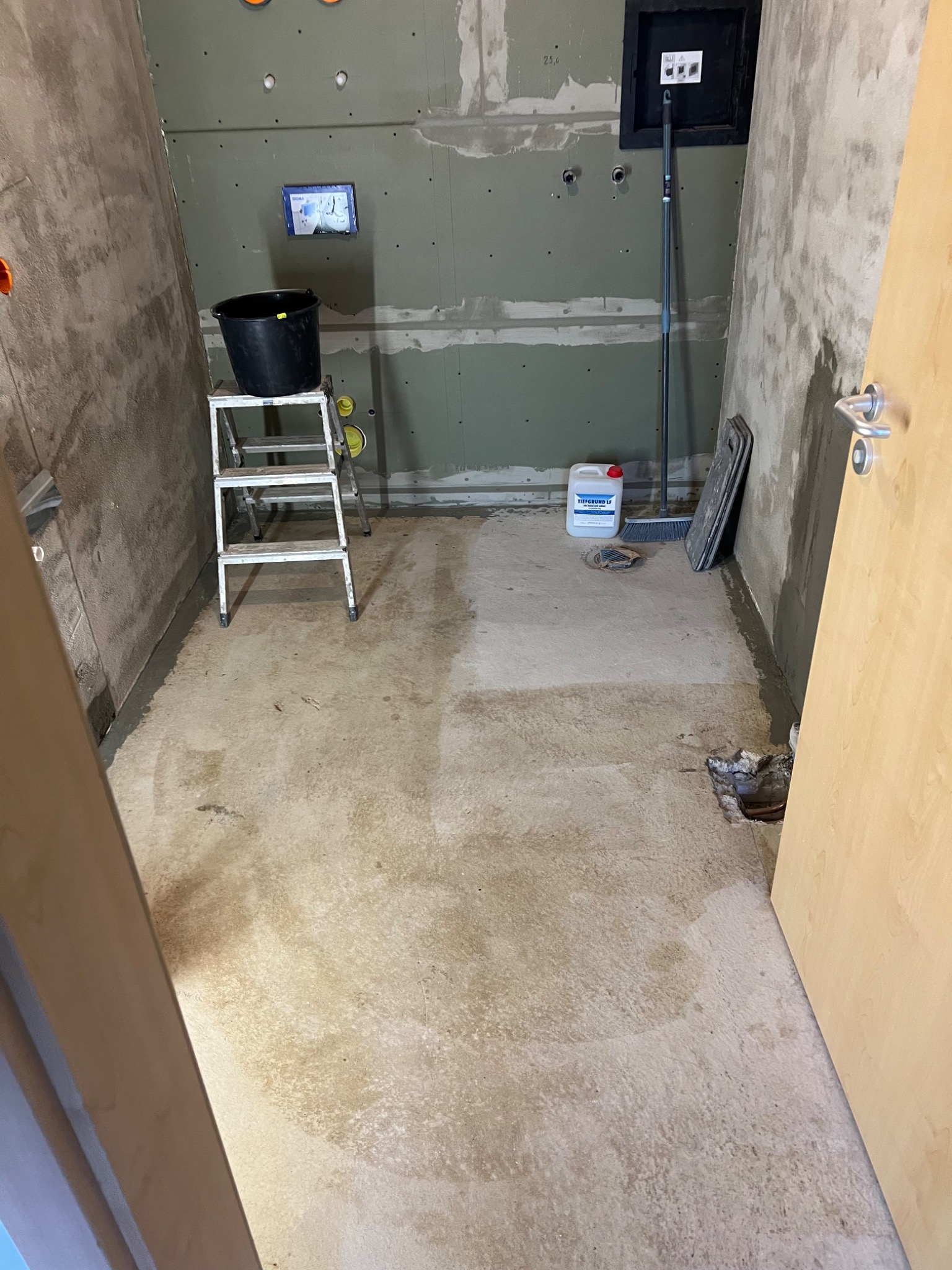 Przygotowanie do prac wykończeniowych w łazience: ściany z płyt karton-gips, grunt, drabina, wiadro, narzędzia. Widoczne instalacje i otwory pod armaturę.