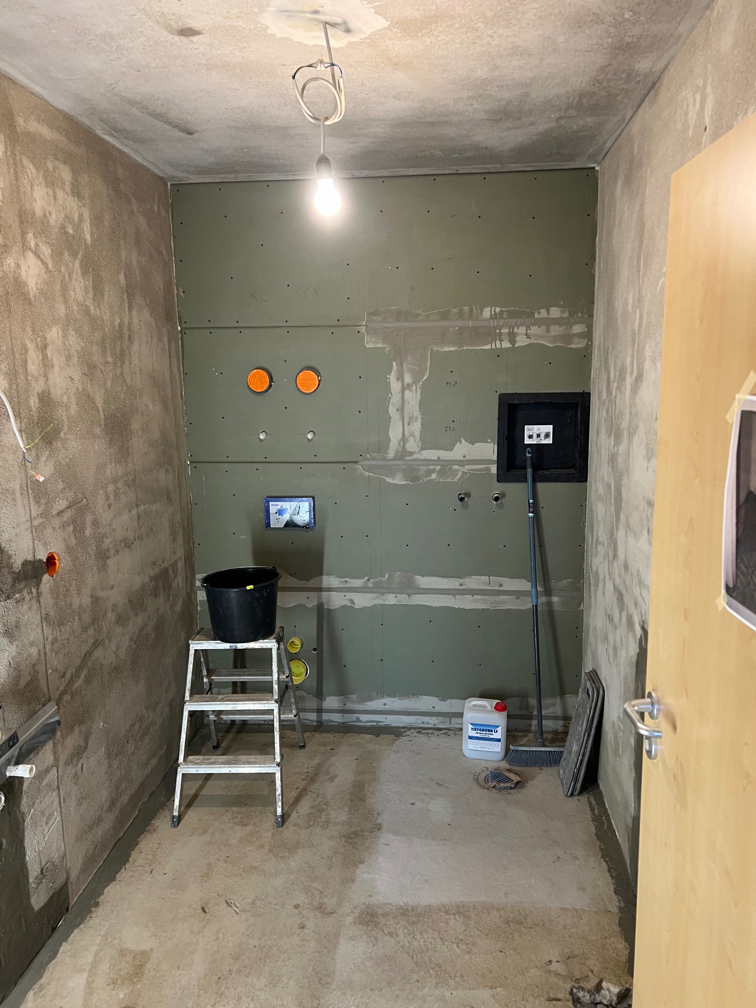 Łazienka w trakcie prac: ściany z płyt gipsowo-kartonowych, widoczne instalacje, drabina, wiadro i preparat gruntujący. Surowy stan, przygotowanie do dalszych prac wykończeniowych.