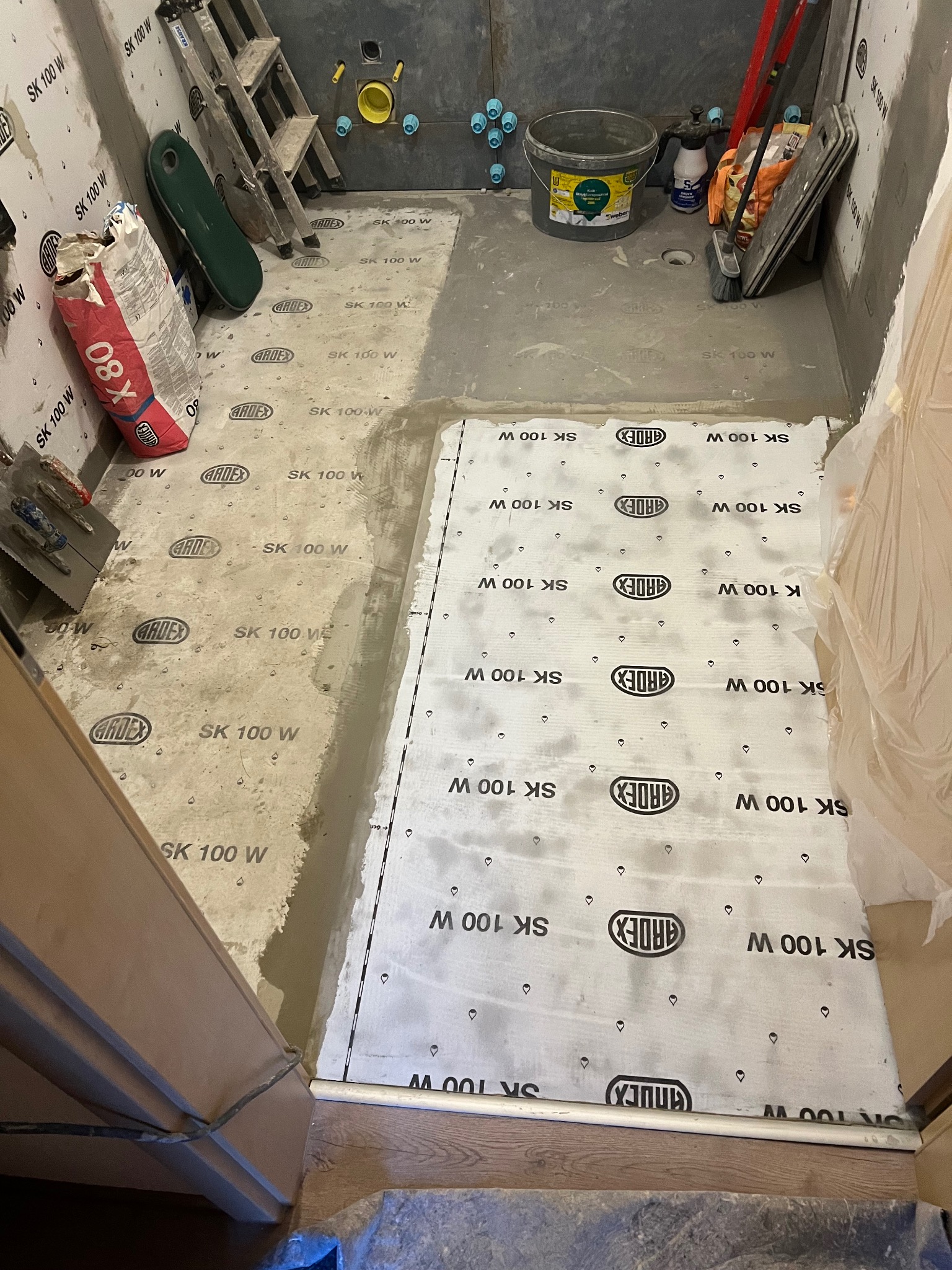 Przygotowanie podłoża w łazience: częściowo wylany beton, mata hydroizolacyjna Ardex SK 100 W, drabina, wiadro Weber. Etap prac przed wykończeniem.