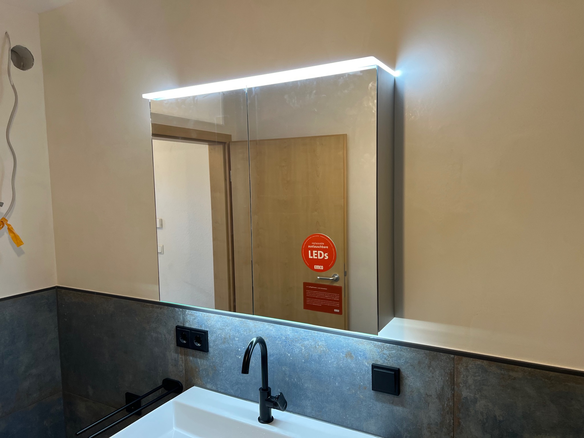 Nowoczesna łazienka w Owidzu z lustrem z podświetleniem LED, czarną armaturą i szarą okładziną. Widoczne detale wykończenia.