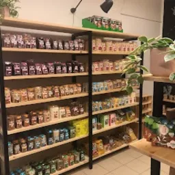 P&oacute;łki sklepowe wypełnione r&oacute;żnorodnymi produktami spożywczymi w słoikach i opakowaniach, ustawione na drewnianych regałach z czarną metalową ramą. Widoczne są r&oacute;żne kolory etykiet i zawartości...