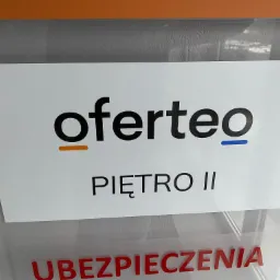 Tabliczka informacyjna z logo Oferteo i napisem 'PIĘTRO II', widoczny fragment napisu 'UBEZPIECZENIA' poniżej.