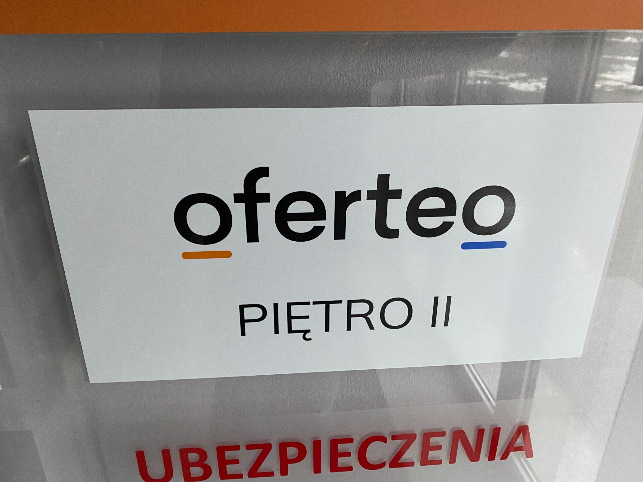 Tabliczka informacyjna z logo Oferteo i napisem 'PIĘTRO II', widoczny fragment napisu 'UBEZPIECZENIA' poniżej.
