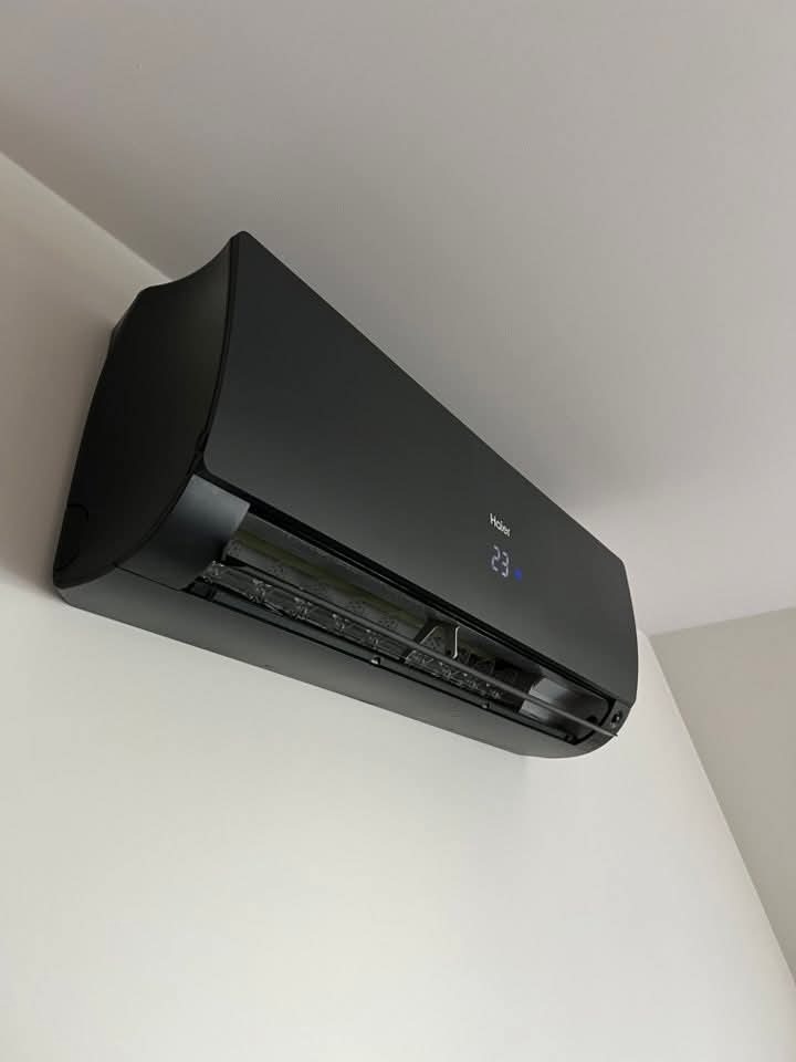 Czarna klimatyzacja Haier zamontowana na białej ścianie, widoczny wyświetlacz temperatury. Minimalistyczny design, nowoczesne wnętrze.