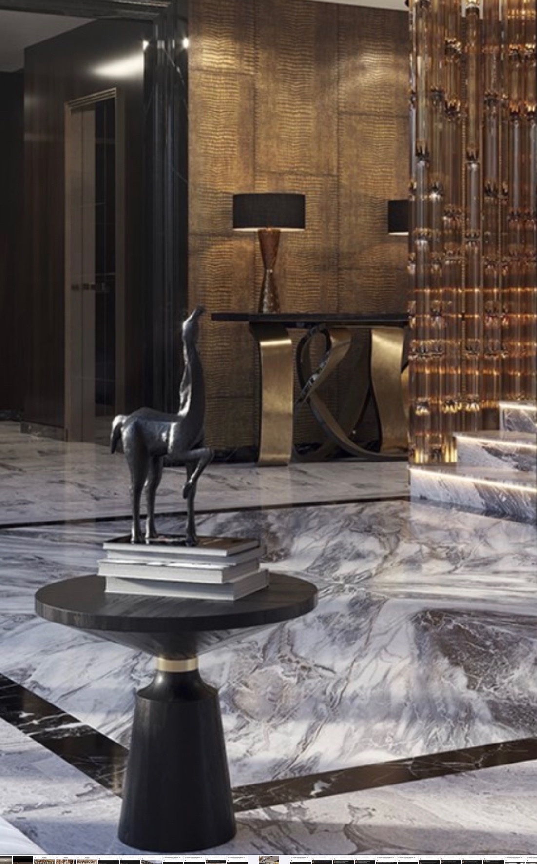 Eleganckie wnętrze z marmurową podłogą, stolikiem z czarnym blatem, rzeźbą konia na książkach, złotymi akcentami na konsoli i dekoracyjną ścianką z rurek.