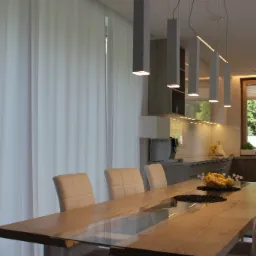 Nowoczesna aranżacja kuchni z jadalnią w Złotokłosie: drewniany stół z szklanym blatem, minimalistyczne lampy wiszące i krzesła w odcieniach bieli.