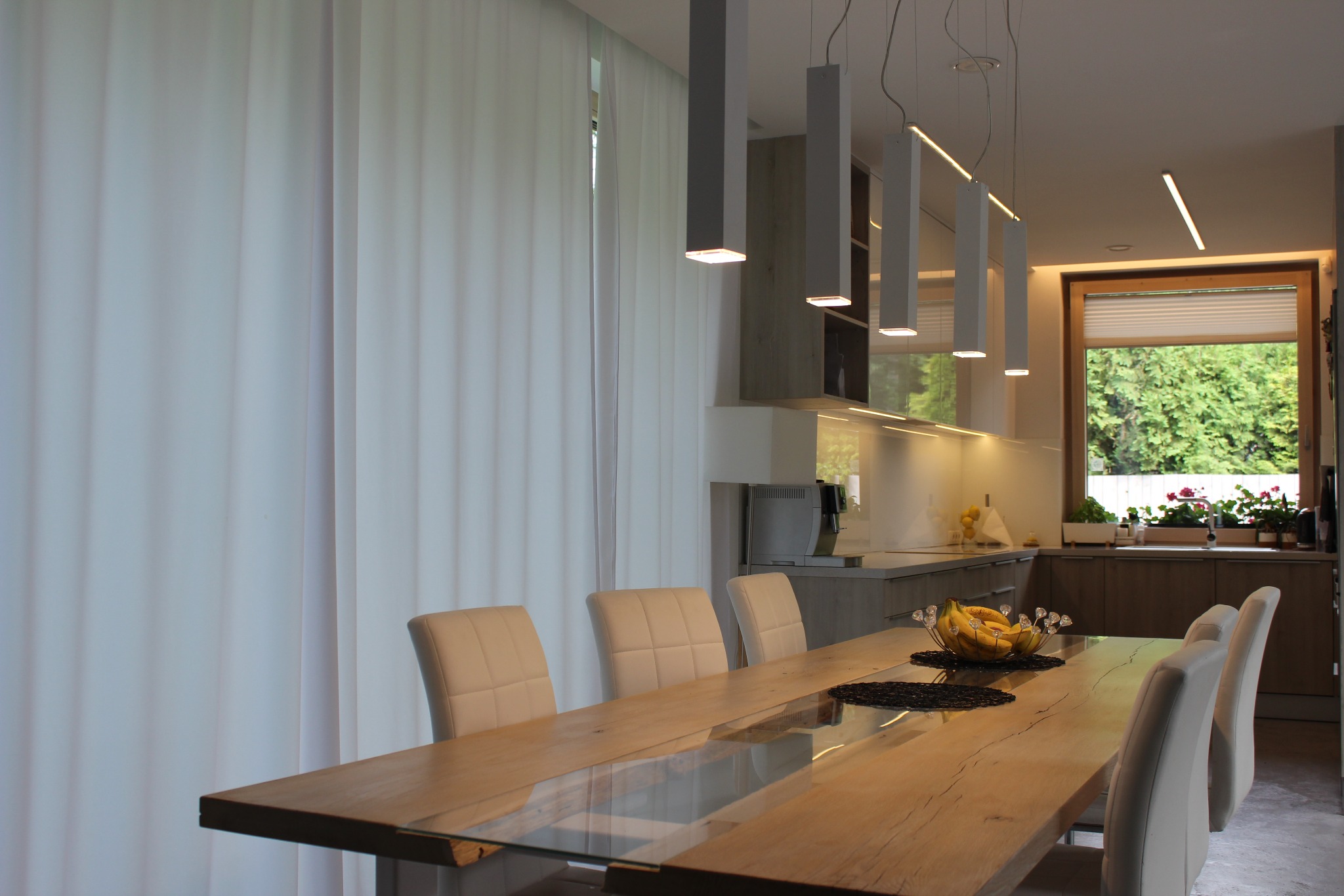Nowoczesna aranżacja kuchni z jadalnią w Złotokłosie: drewniany stół z szklanym blatem, minimalistyczne lampy wiszące i krzesła w odcieniach bieli.