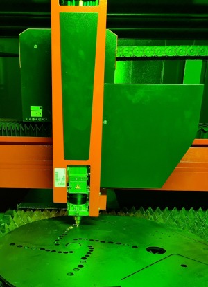 Proces cięcia blachy grubym laserem przemysłowym w hali produkcyjnej, oświetlenie w odcieniach zieleni.