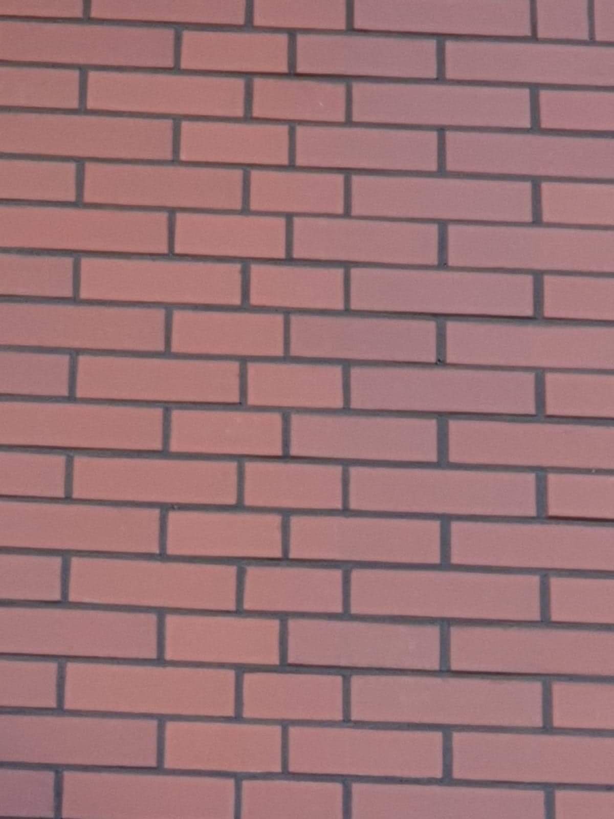 Fragment ściany z czerwonej cegły ułożonej w regularny wzór z ciemnoszarą fugą.