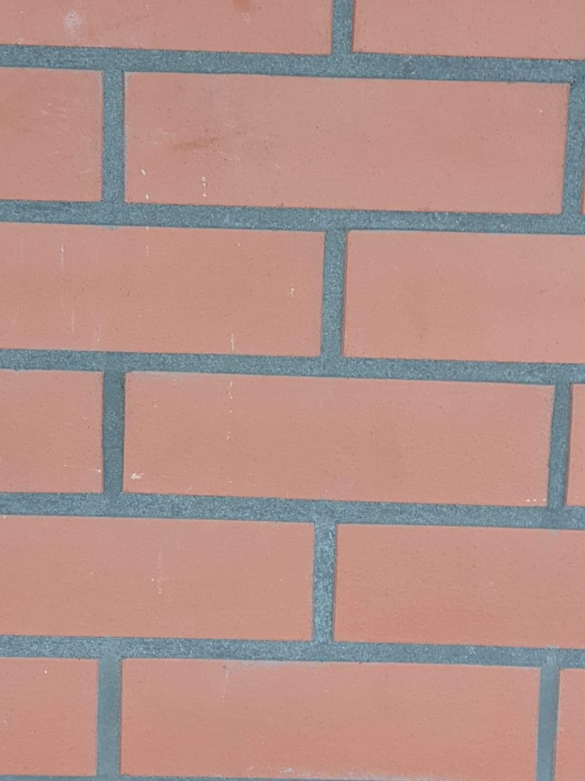 Fragment muru z czerwonej cegły połączonej szarą zaprawą, widoczne niedoskonałości na powierzchni cegieł.
