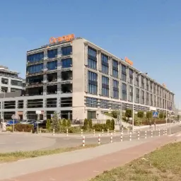 Panorama biurowców z logo Orange na dachu, widok z poziomu ulicy w słoneczny dzień.