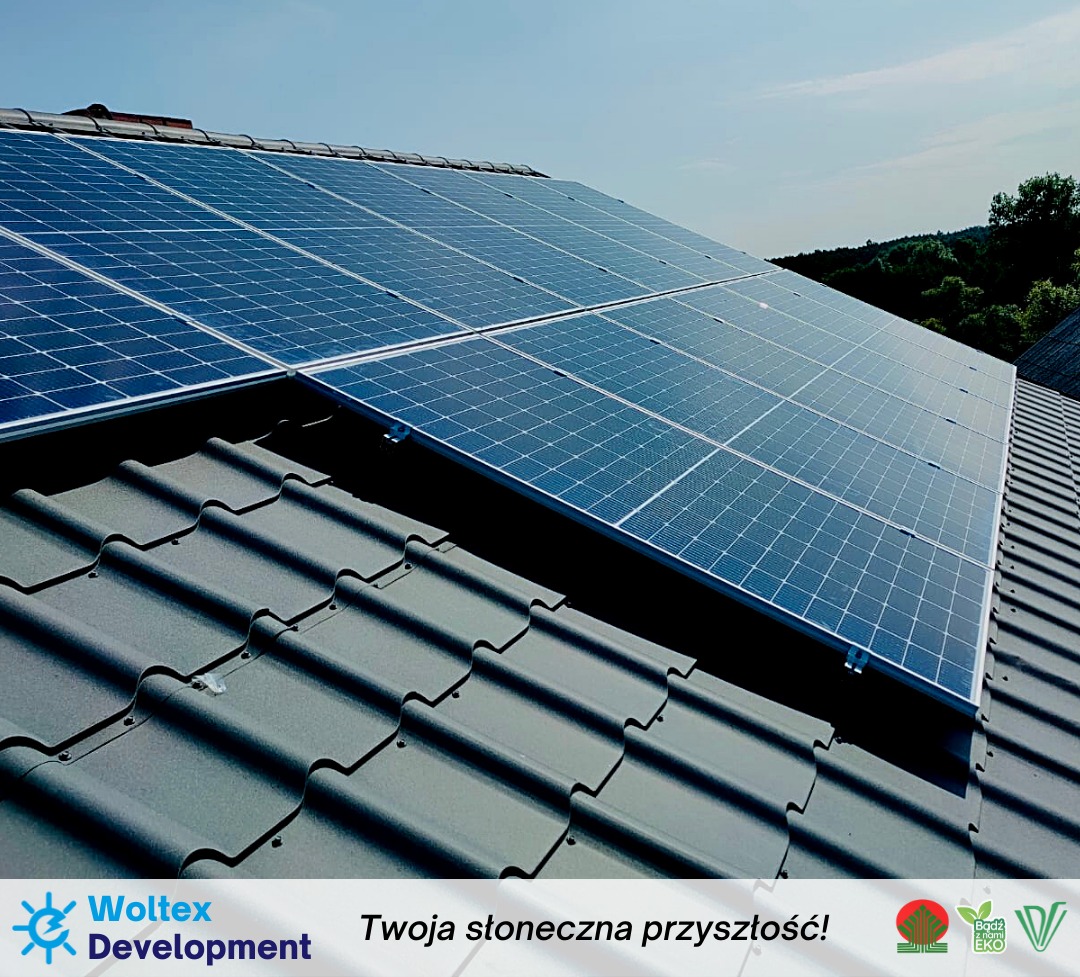 Panele słoneczne zamontowane na ciemnoszarym dachu z dachówki ceramicznej, widok z dołu pod kątem w słoneczny dzień, logo firmy w dolnej części kadru.