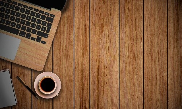 Laptop z drewnianą obudową, notes, długopis i filiżanka kawy na drewnianym biurku.