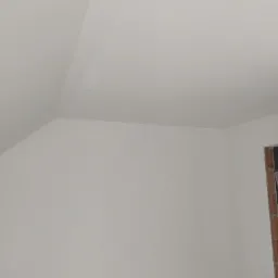 Pomalowane na biało poddasze z widocznym fragmentem otworu okiennego z ceglaną obramówką.