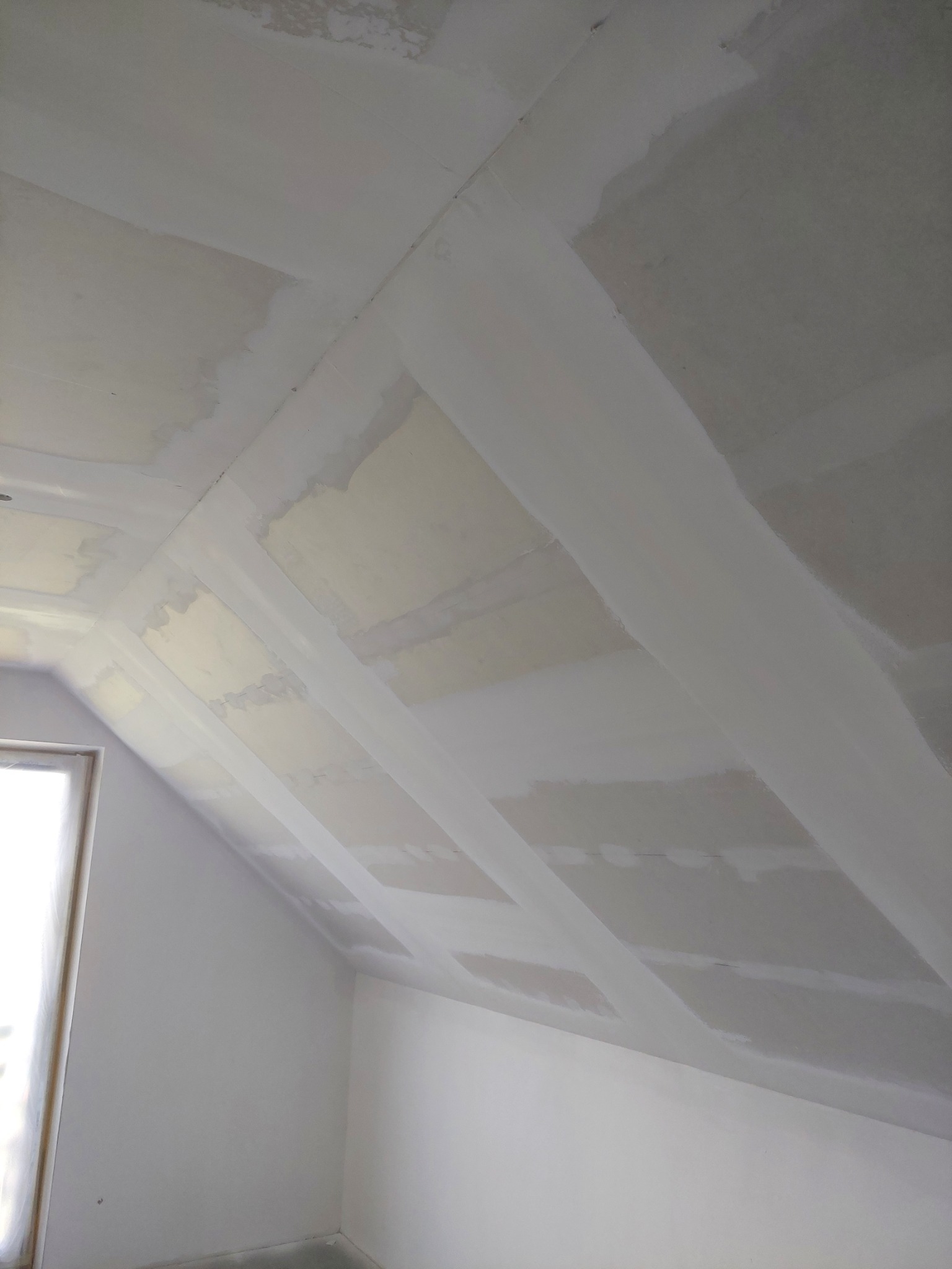 Poddasze w trakcie prac wykończeniowych: szpachlowane łączenia płyt gipsowo-kartonowych na skośnym suficie, widoczne nierówności i przygotowanie do malowania.