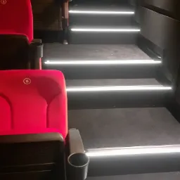 Czerwone fotele kinowe z numerem 6 i podświetlane stopnie schodów w ciemnym wnętrzu.