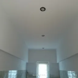 Wnętrze po świeżym odmalowaniu: białe ściany i sufit z trzema wbudowanymi punktami świetlnymi, widoczne ślady prac wykończeniowych przy oknie i dolnej części ścian.