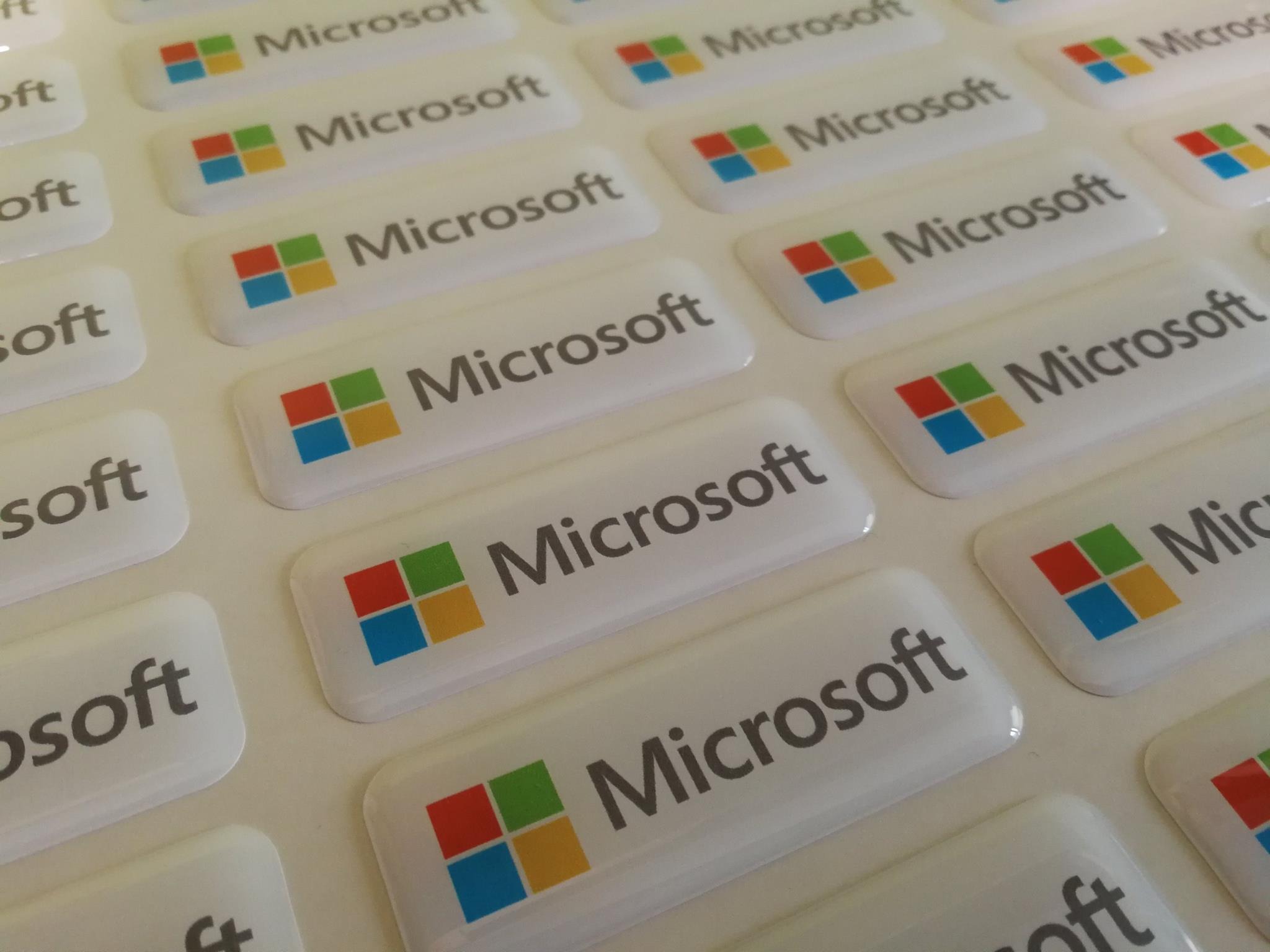 Arkusz z naklejkami z logo Microsoft, wykonane z połyskliwego materiału z zaokrąglonymi rogami, ułożone równo na białym tle.