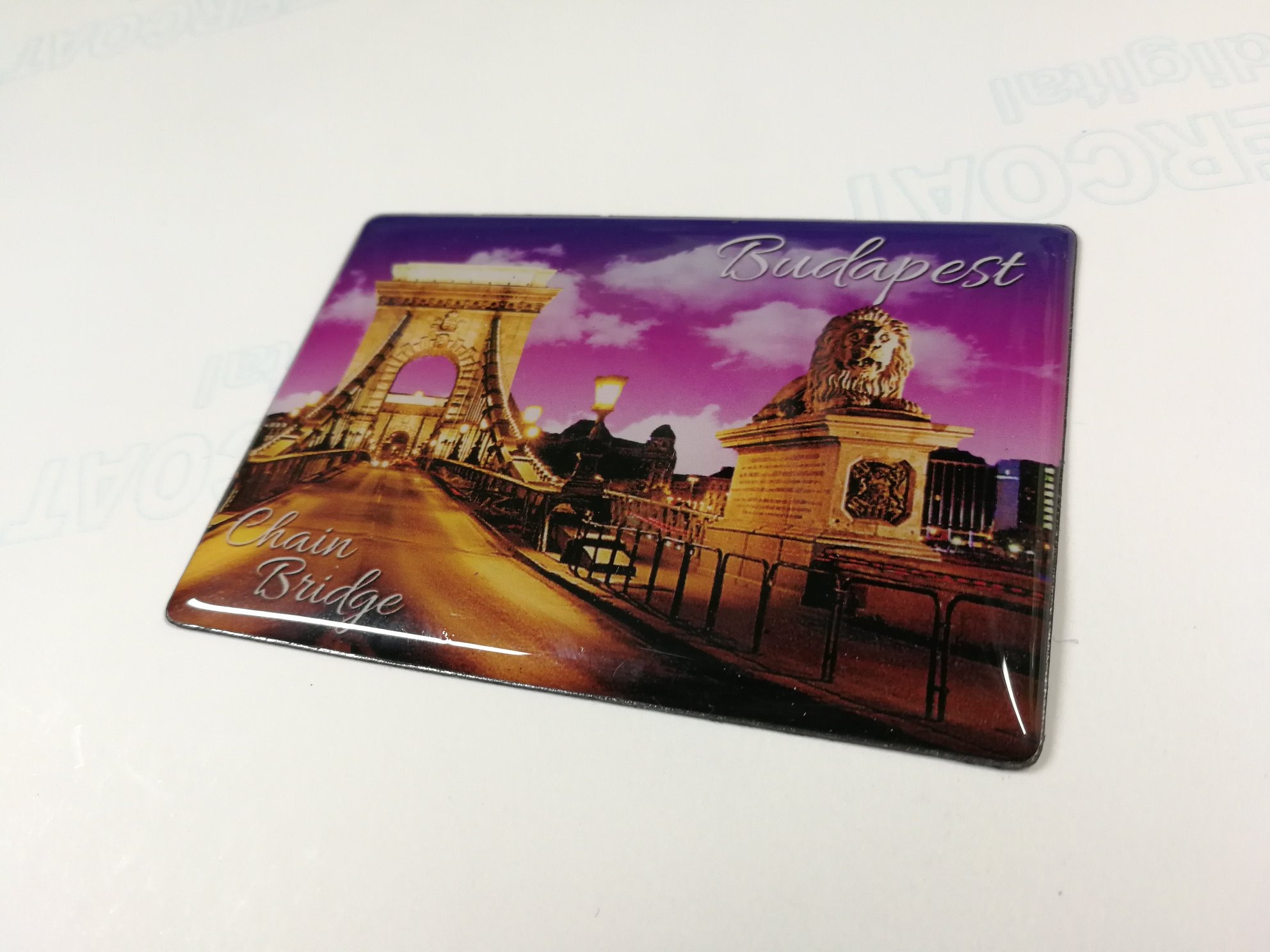 Błyszcząca naklejka przedstawiająca most Széchenyi w Budapeszcie z lwem na tle fioletowego nieba.