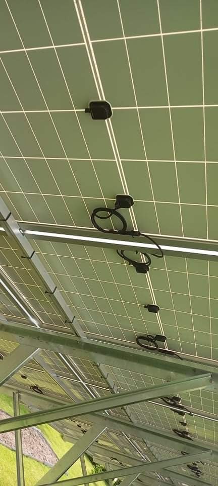 Widok od spodu na panele z zielonymi ogniwami, przymocowane do metalowej konstrukcji nośnej z widocznymi przewodami i złączami.