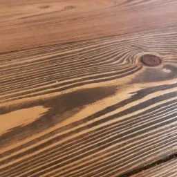 Fragment deski podłogowej z widocznym usłojeniem i sękiem, po zabiegu szczotkowania i bejcowania na ciemny kolor uwydatniający strukturę drewna.