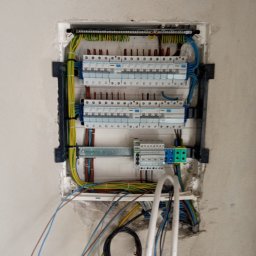 Perfekt Instal - Otwarta skrzynka bezpiecznikowa w surowej ścianie, widoczne liczne przewody i zabezpieczenia, praca w trakcie wykonywania.