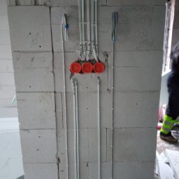 Perfekt Instal - Surowa ściana z betonu komórkowego z widoczną instalacją elektryczną w peszlach i puszkach instalacyjnych, częściowo zamontowaną, z notatkami ołówkiem na ścianie.