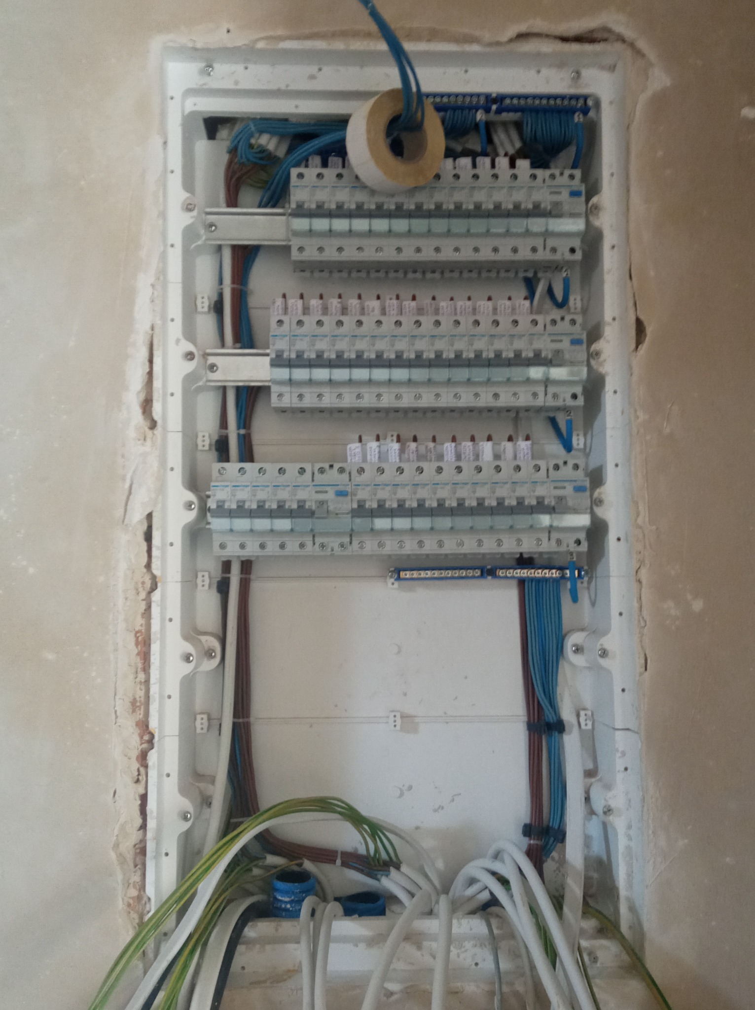 Rozdzielnica elektryczna w trakcie montażu w ścianie, widoczne kable i zabezpieczenia, ściana w stanie surowym.