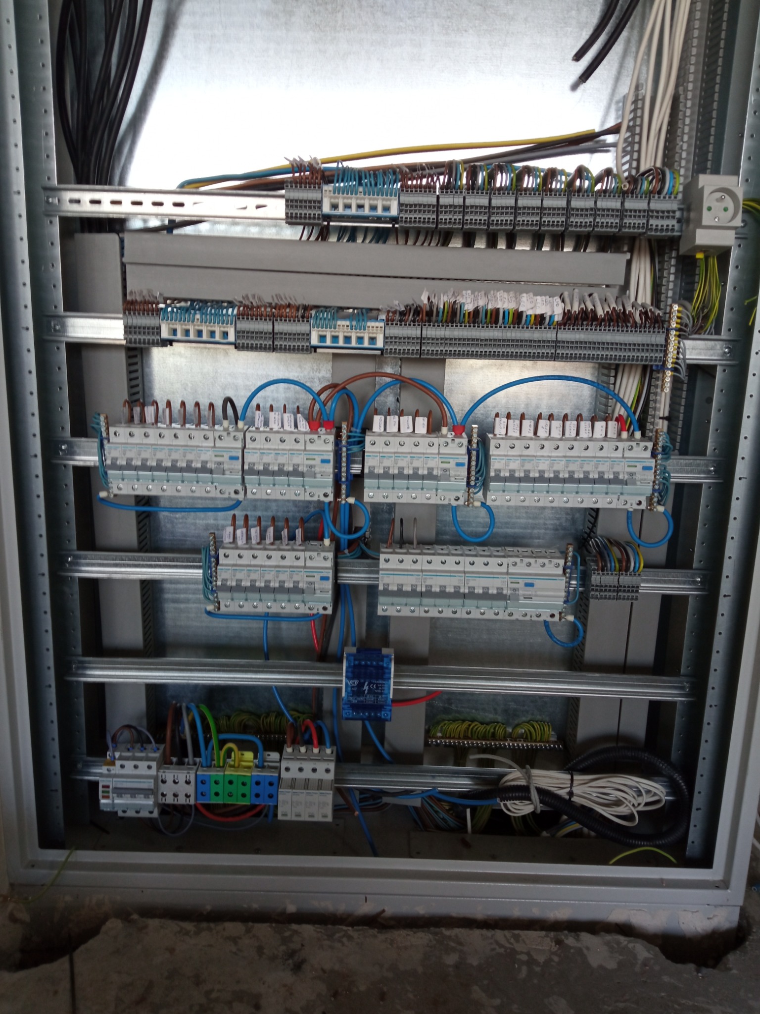 Wnętrze szafy elektrycznej z zamontowanymi bezpiecznikami, przewodami i listwami zaciskowymi, widoczne kable w różnych kolorach i grubościach, schludnie ułożone w metalowej obudowie.