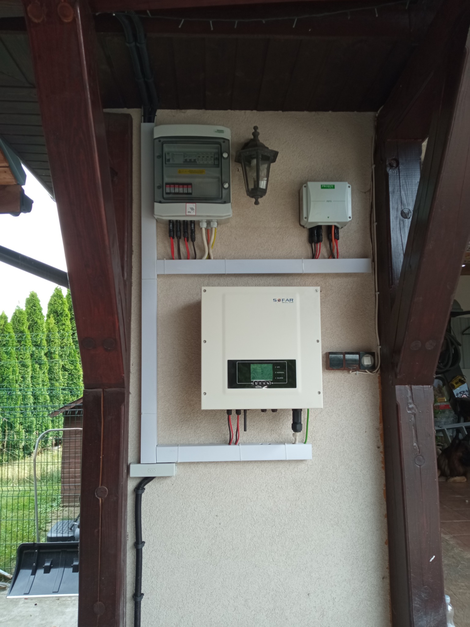 Instalacja fotowoltaiczna: inwerter Sofar, rozdzielnica i zabezpieczenia, zamontowane na ścianie budynku z drewnianą konstrukcją werandy.