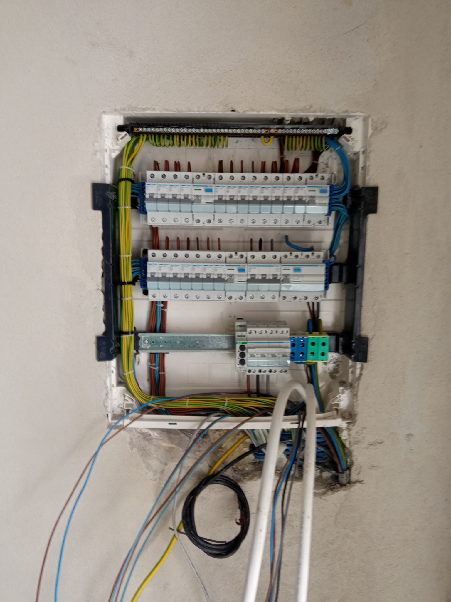 Otwarta skrzynka bezpiecznikowa w surowej ścianie, widoczne liczne przewody i zabezpieczenia, praca w trakcie wykonywania.