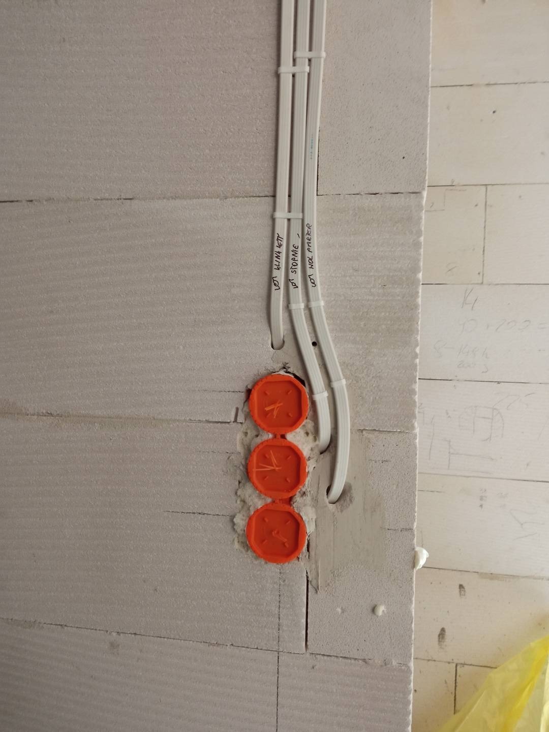 Białe kable elektryczne przymocowane do surowej ściany z betonu komórkowego, z trzema pomarańczowymi puszkami instalacyjnymi.