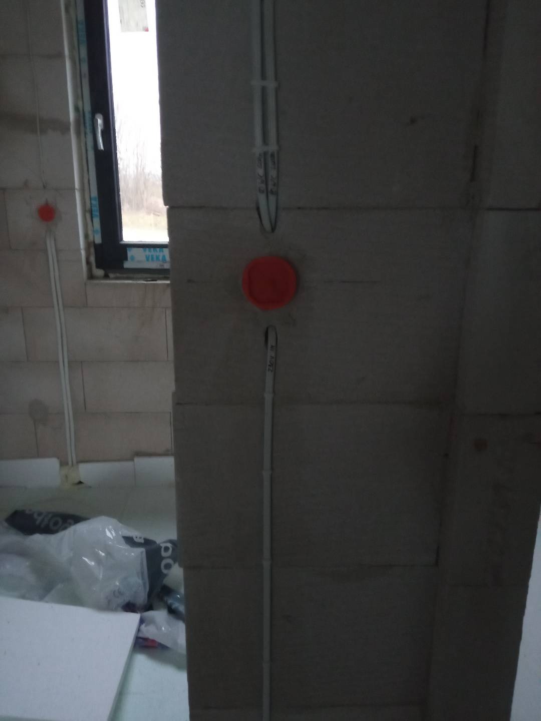 Surowe ściany z betonu komórkowego z widocznymi, białymi przewodami elektrycznymi prowadzonymi w peszlach i puszkach instalacyjnych w kolorze pomarańczowym, widoczne elementy instalacji...