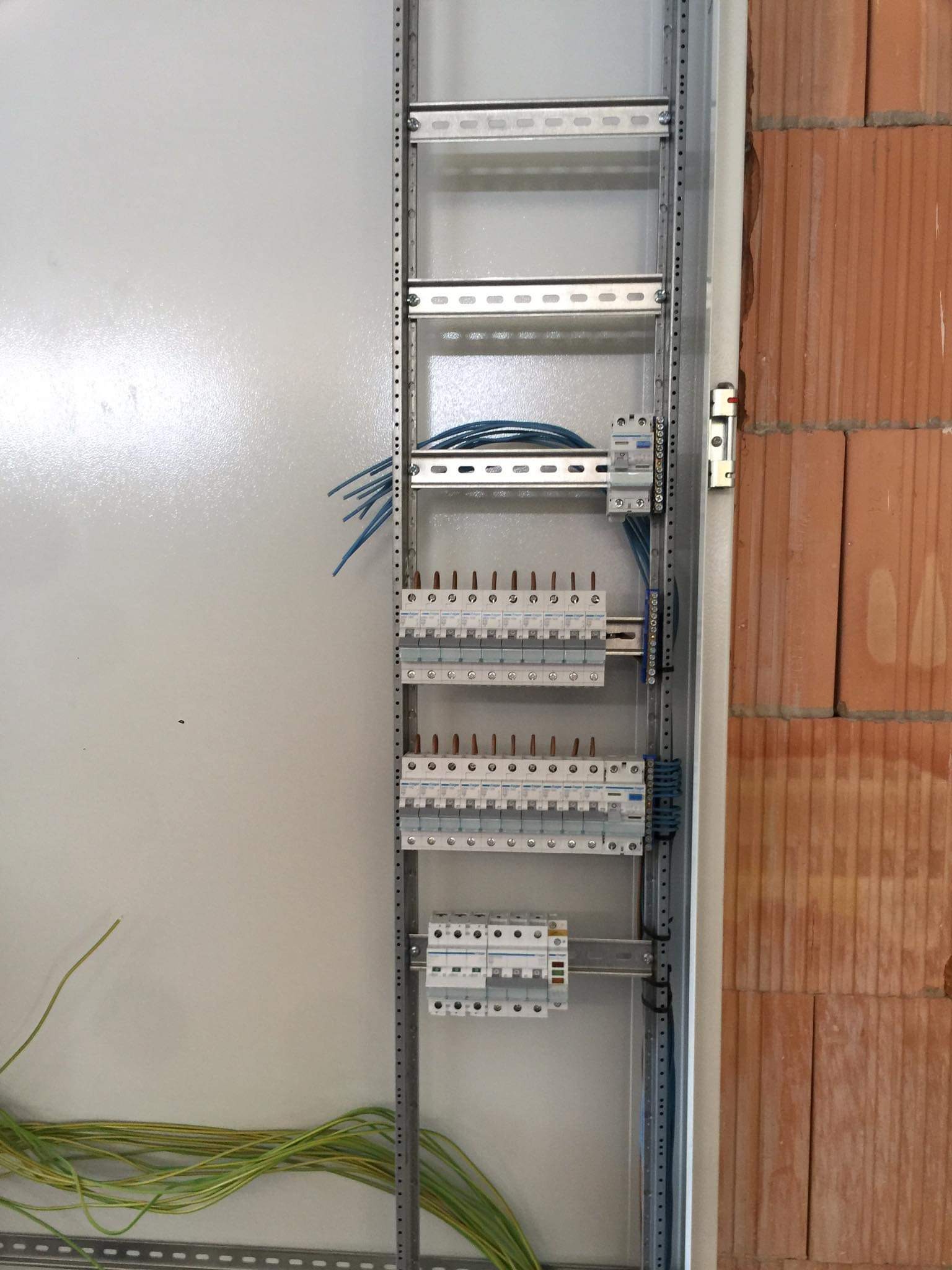 Rozdzielnica elektryczna w trakcie montażu, widoczne kable i zabezpieczenia, ściana z cegły dziurawki w tle.