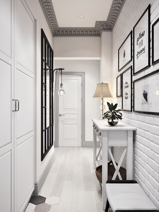 Biały przedpokój w stylu skandynawskim z ceglaną ścianą, dekoracyjną konsolą, lustrem z czarnymi szprosami i heksagonalną posadzką przy wejściu.