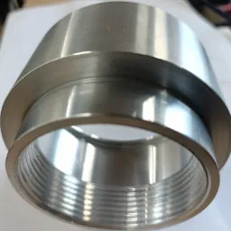 Szczegółowe ujęcie gwintowanego, metalowego elementu cylindrycznego z kołnierzem, obrobionego z dużą precyzją, leżącego na białej powierzchni.