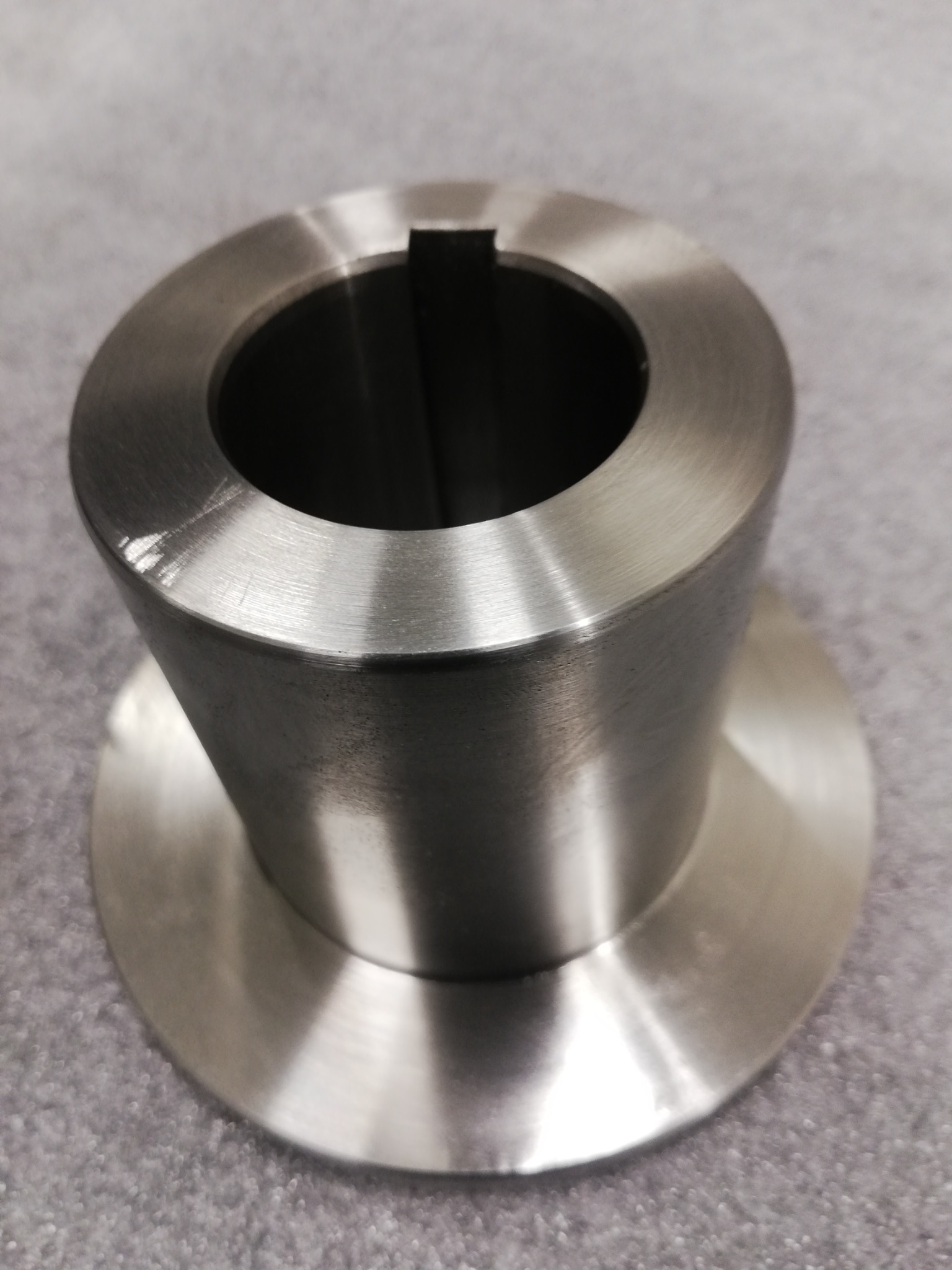 Precyzyjnie obrobiony, metalowy element z kołnierzem i rowkiem wpustowym, widoczne ślady obróbki skrawaniem na powierzchni.