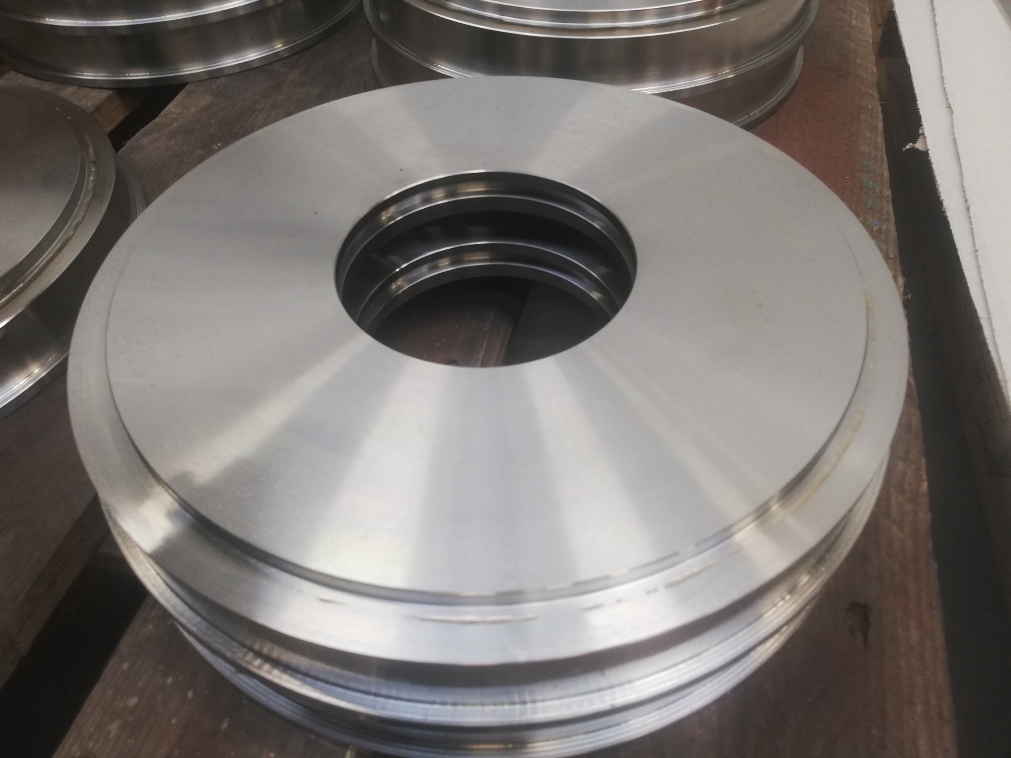 Stos obrobionych metalowych pierścieni z centralnym otworem, leżących na drewnianej powierzchni. Widoczne ślady obróbki.