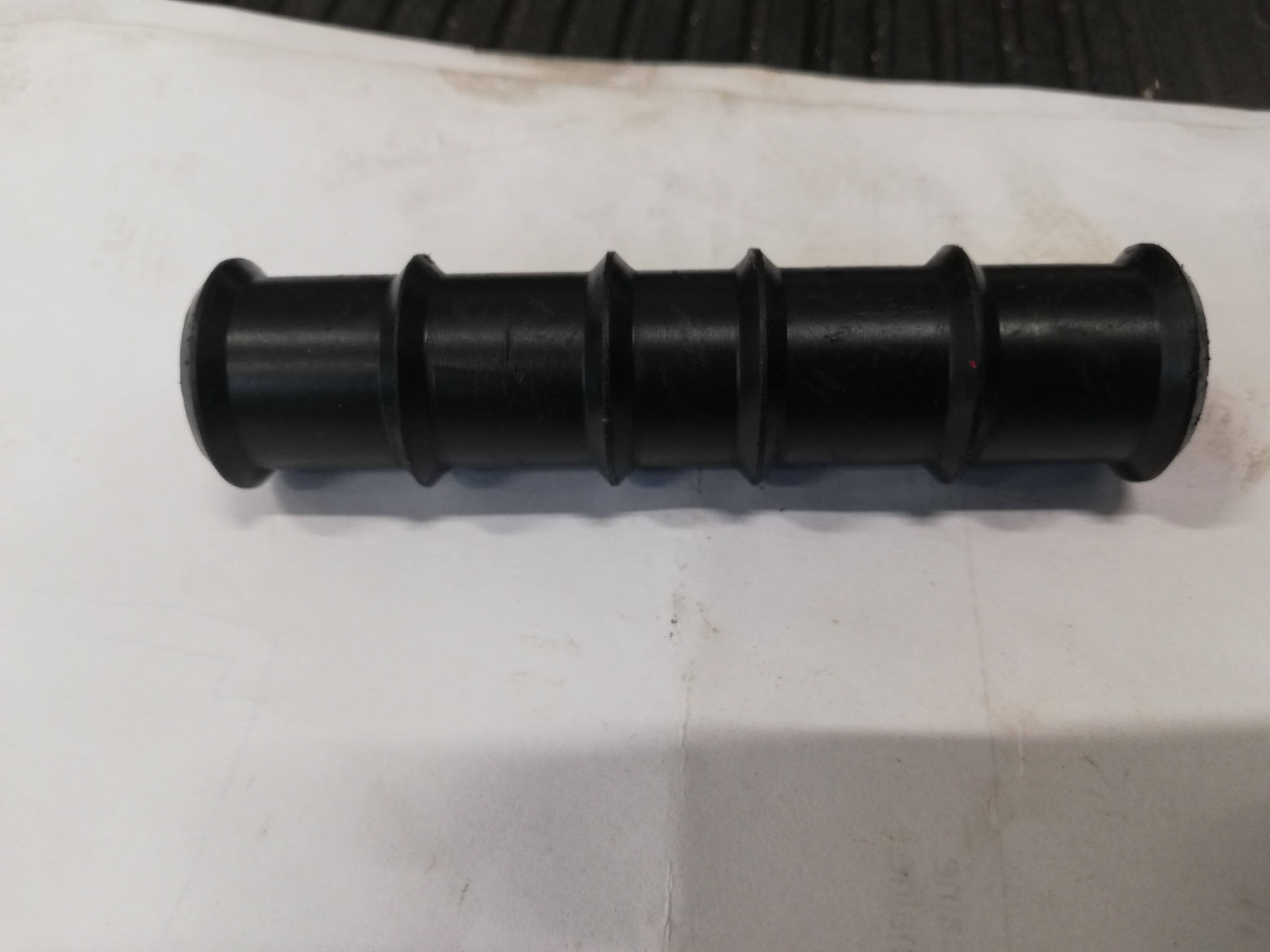 Czarny, gumowy element z trzema pierścieniowymi rowkami, leżący na białym tle.