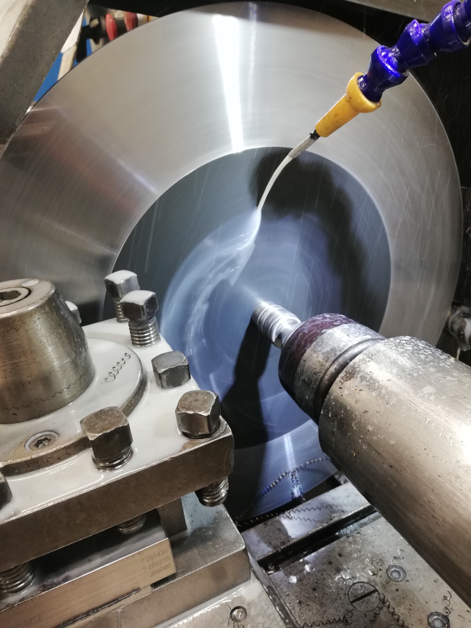 Metalowa tarcza obrabiana na tokarce z użyciem chłodziwa, widoczne wióry i metalowe elementy maszyny.