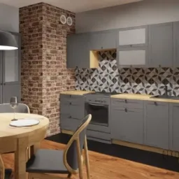 Szara kuchnia z ceglanym filarem, okrągłym drewnianym stołem z nakryciem i geometrycznymi płytkami nad blatem.