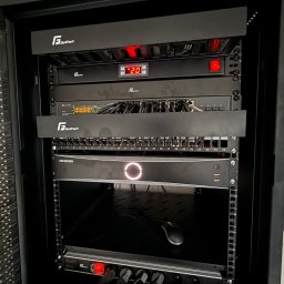 Instalacje Techniczne Sławno - Szafa rack z zainstalowanymi urządzeniami sieciowymi i do monitoringu, w tym rejestratorem Hikvision z podświetlonym logo, routerem TP-Link z diodami oraz listwą zasilającą GetFort z włączonym...