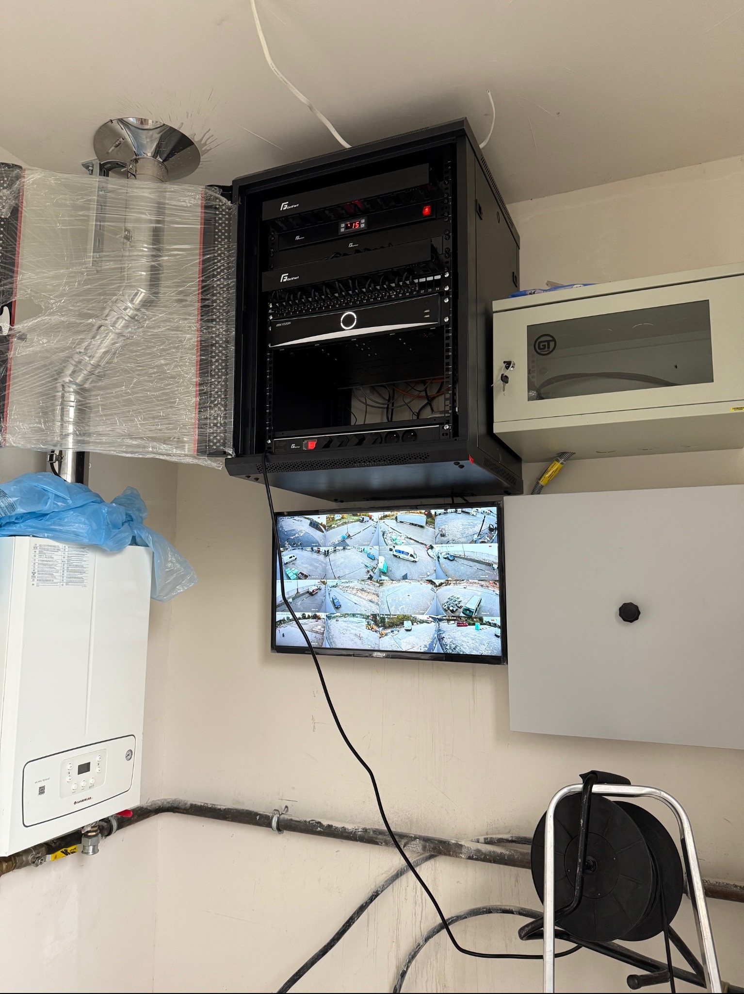 Centrum monitoringu z serwerem, ekranem podglądu z kamer i okablowaniem, obok piec gazowy w folii ochronnej.