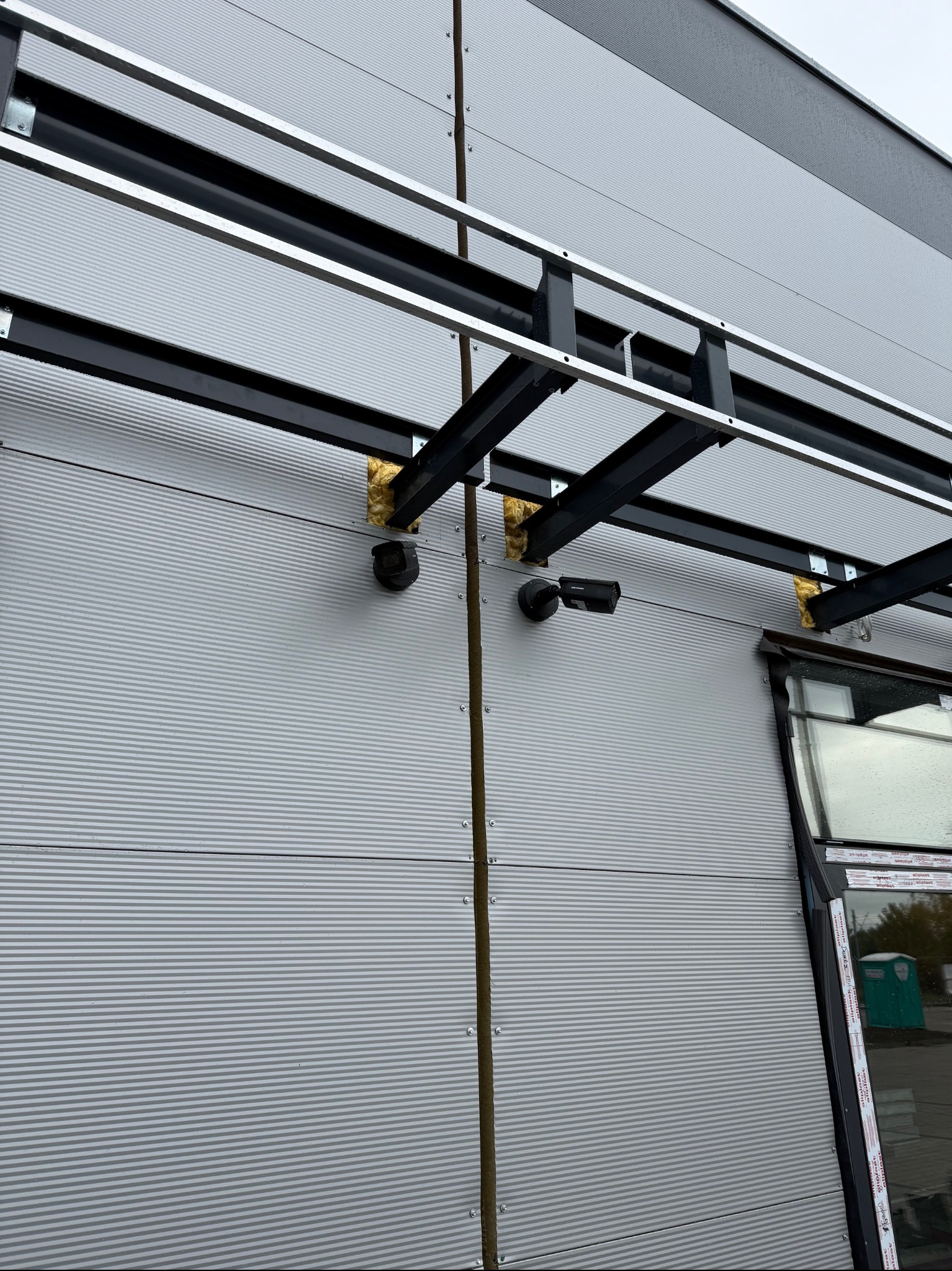 Kamera Hikvision zamontowana na elewacji hali przemysłowej, widoczne mocowania i fragment okna.